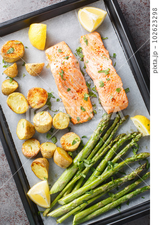 Homemade salmon fillet baked with asparagus and new potatoes with herbs and lemon close-up in a baking sheet. vertical top vew 102623298