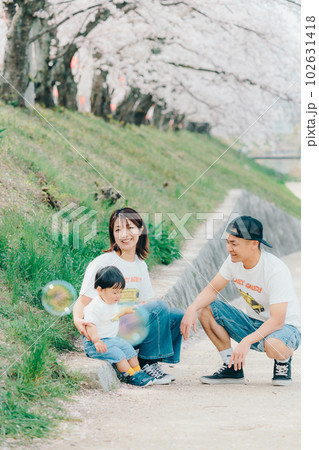桜の木の下で佇む家族3人の写真 102631418