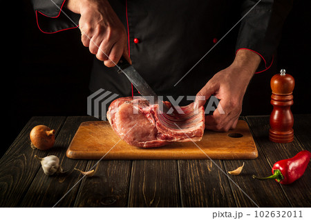 For a fire, raw ribs must be cut into small pieces. Hands of a butcher with a knife in the kitchen. Cooking delicious food for the hotel. For a fire, raw ribs must be cut into small pieces. Hands of a butcher with a knife in the kitchen. Cooking delicious food for the hotel. 102632011