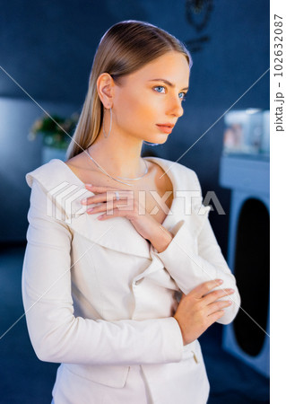 Adoarable beautiful model stands in mirror in a jewelry store tries on a gold diamond necklace that sparkles on the girl. Girl is adorned with golden jewelry and diamonds in a luxurious boutique. 102632087