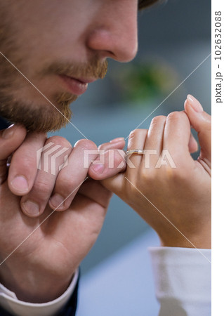 Man in a suit holding hand his bride in a jewelry store, tenderly kissing. Girl tries on a gold diamond high heel in a luxurious and expensive boutique. The loving couple is in a store with gold. Man in a suit holding hand his bride in a jewelry store, tenderly kissing. Girl tries on a gold diamond high heel in a luxurious and expensive boutique. The loving couple is in a store with gold. 102632088