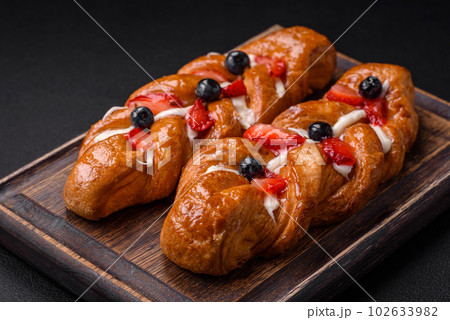 Delicious fresh crispy pastry in the form of a pigtail with strawberries and blueberries Delicious fresh crispy pastry in the form of a pigtail with strawberries and blueberries 102633982