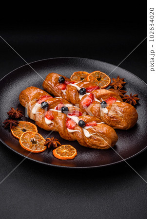 Delicious fresh crispy pastry in the form of a pigtail with strawberries and blueberries Delicious fresh crispy pastry in the form of a pigtail with strawberries and blueberries 102634020
