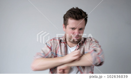 The European young man nervously scratches his hands. He has an allergy, and the itching bothers him The European young man nervously scratches his hands. He has an allergy, and the itching bothers him 102636839