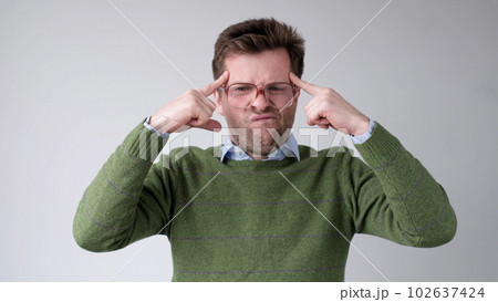 European young man holds his fingers to his temple trying to concentrate and come up with a plan European young man holds his fingers to his temple trying to concentrate and come up with a plan 102637424