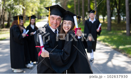 A group of graduates in robes outdoors. An elderly man and a young woman congratulate each other on their graduation. A group of graduates in robes outdoors. An elderly man and a young woman congratulate each other on their graduation. 102637930