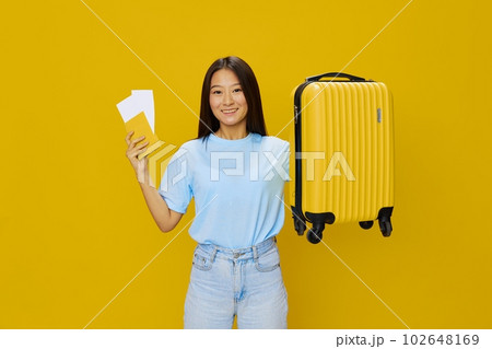Asian woman traveling with yellow suitcase and tickets with passport in hand, tourist traveling by plane and train with luggage on yellow background in blue T-shirt and jeans 102648169