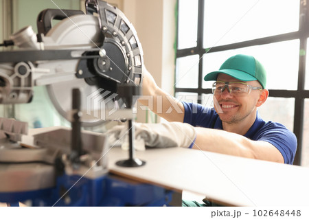 Smiling employee cuts wooden board with sawing machine Smiling employee cuts wooden board with sawing machine 102648448