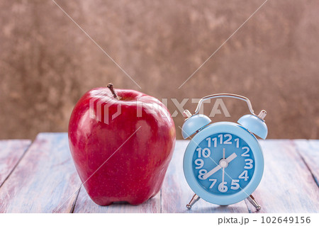 Apple and alarm clock on wood table at the morning. Apple and alarm clock on wood table at the morning. 102649156