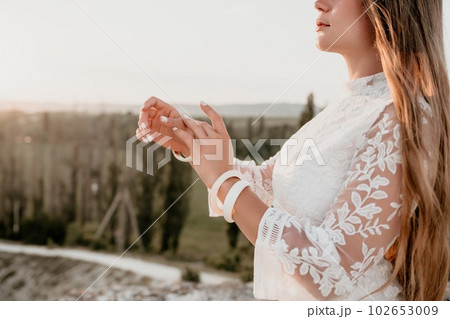 Happy woman in white boho dress on sunset in mountains. Romantic woman with long hair standing with her back on the sunset in nature in summer with open hands. Silhouette. Nature. Sunset. Happy woman in white boho dress on sunset in mountains. Romantic woman with long hair standing with her back on the sunset in nature in summer with open hands. Silhouette. Nature. Sunset. 102653009