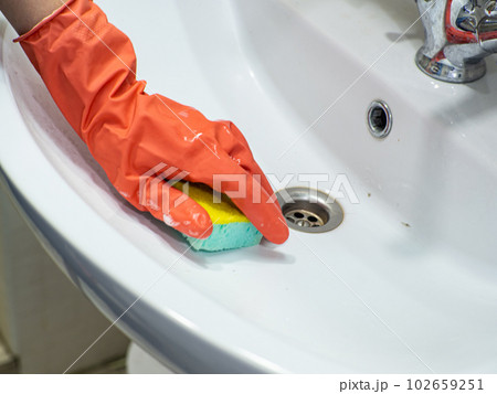 Person hand holding a mint sponge for cleaning bathroom sink and faucet Person hand holding a mint sponge for cleaning bathroom sink and faucet 102659251