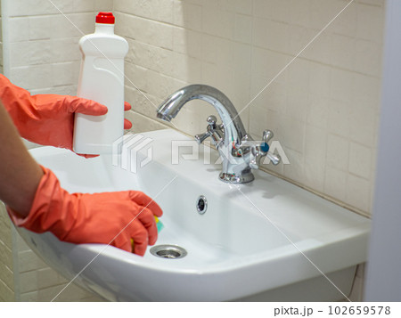 Person hand holding a detergent in white bottle for cleaning bathroom sink Person hand holding a detergent in white bottle for cleaning bathroom sink 102659578