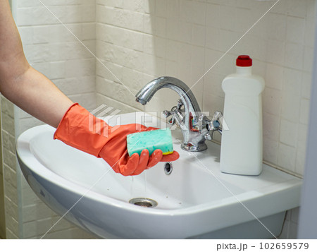 Person hand holding a mint sponge and washing it under water Person hand holding a mint sponge and washing it under water 102659579