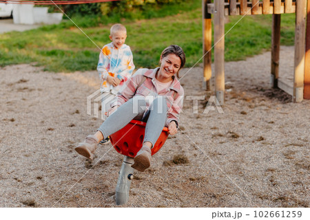 Mother and son having fun on a swing. Motherhood and childhood concept. Sunny summer day. Beautiful family is having fun outside. Parents with children riding on a swing. Mom is playing with her 102661259