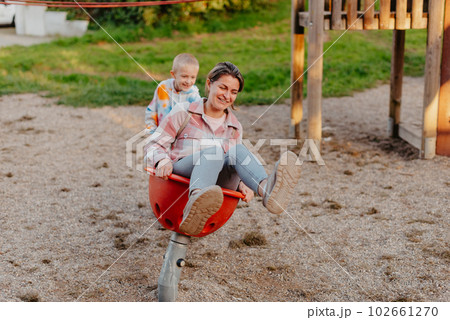 Mother and son having fun on a swing. Motherhood and childhood concept. Sunny summer day. Beautiful family is having fun outside. Parents with children riding on a swing. Mom is playing with her 102661270
