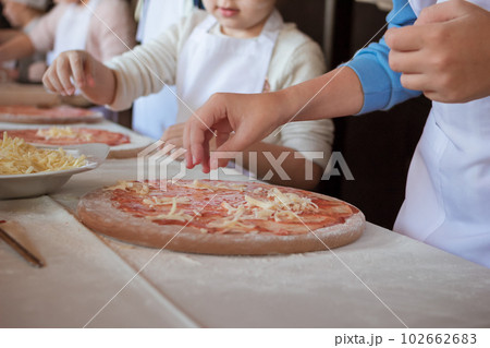 Hand puts cheese on a row pizza on a wooden cutting board sprinkled with flour Hand puts cheese on a row pizza on a wooden cutting board sprinkled with flour 102662683