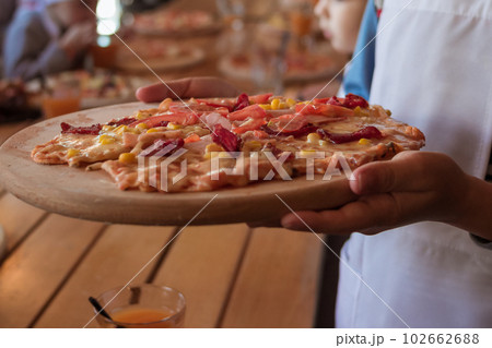 Womans hand holding pizza on a wooden cutting board sprinkled with flour 102662688