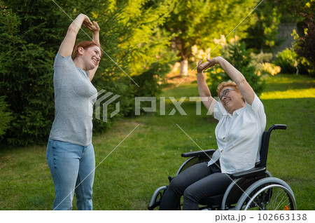 Caucasian woman exercising with elderly mom in wheelchair outdoors.  102663138