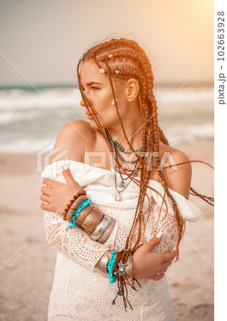 Woman portret sea white dress. Model in boho style in a white long dress and silver jewelry on the beach. Her hair is braided, and there are many bracelets on her arms. Woman portret sea white dress. Model in boho style in a white long dress and silver jewelry on the beach. Her hair is braided, and there are many bracelets on her arms. 102663928