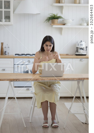 Serious engaged Latin girl talking on video call on laptop 102664403