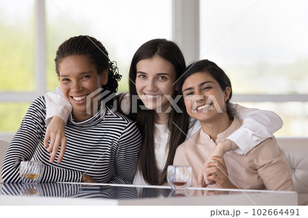 Three multiethnic women hugging smiling, staring at camera 102664491