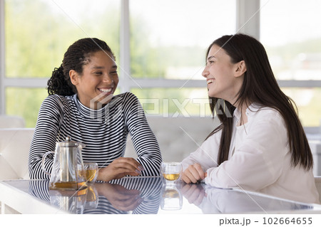 Two pretty millennial women talking seated at table in cafe 102664655