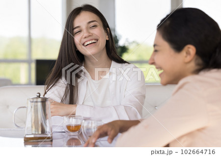 Caucasian and Indian girls enjoy chat drinking tea in cafe Caucasian and Indian girls enjoy chat drinking tea in cafe 102664716
