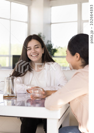 Two cheerful multiethnic girls laughing sit at table in cafe 102664893