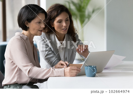 Two businesswomen discuss app or on-line presentation using laptop 102664974