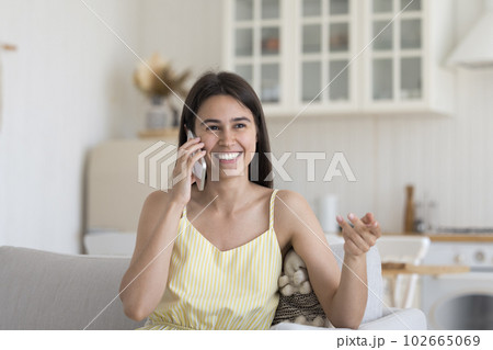 Cheerful Hispanic girl speaking on cellphone, sitting on home couch 102665069