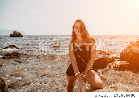 Woman summer travel sea. Happy tourist in hat enjoy taking picture outdoors for memories. Woman traveler posing on the beach at sea surrounded by volcanic mountains, sharing travel adventure journey 102666490