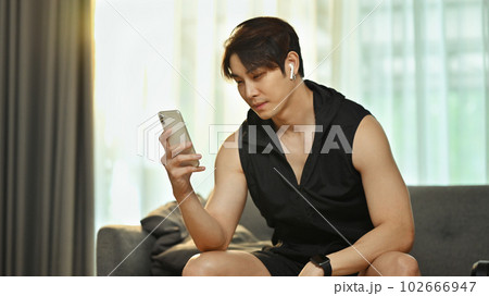 Young asian man in sportswear using smartphone during workout break, watching workout video online Young asian man in sportswear using smartphone during workout break, watching workout video online 102666947
