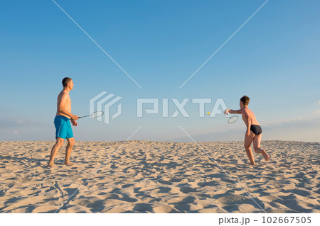 Sports beach games. Boy with his father playing beach badminton on the seashore. 102667505