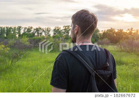 Rear view portrait of a young man in the forest at sunset. A man enjoys nature. Tourism, lifestyle Rear view portrait of a young man in the forest at sunset. A man enjoys nature. Tourism, lifestyle 102667672