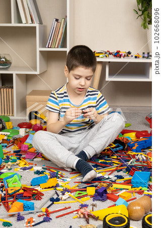 Little boy playing with toys sitting on the floor among scattered toys, a mess in the children's room Little boy playing with toys sitting on the floor among scattered toys, a mess in the children's room 102668096