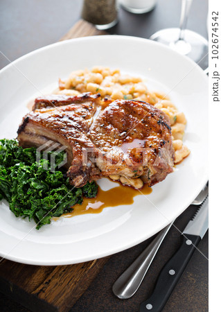 Grilled pork chop with cassoulet and braised greens 102674542