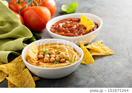 Homemade hummus and tomato salsa in white bowls with chips Homemade hummus and tomato salsa in white bowls with chips 102675264
