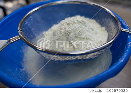 Sifting white flour through a sieve 102679329