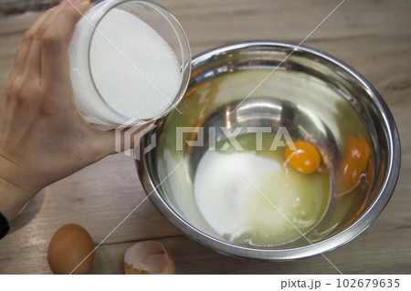 Hand adds sugar to metallic bowl with egg Hand adds sugar to metallic bowl with egg 102679635