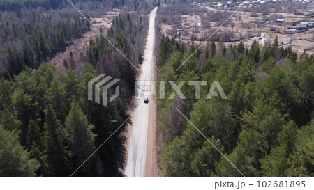 A dark car is driving along a forest road. Vehicle tracking camera. View of the car from a drone. A dark car is driving along a forest road. Vehicle tracking camera. View of the car from a drone. 102681895