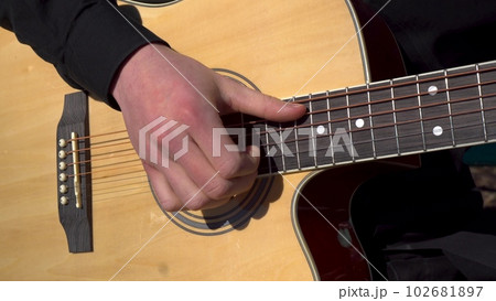 A young man plays the acoustic guitar. Close-up of a hand striking a string. 102681897