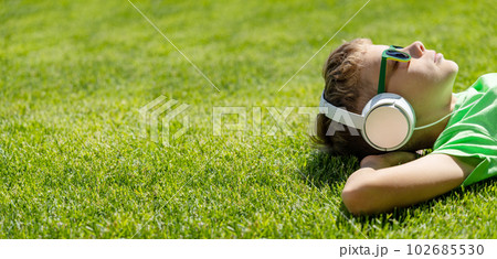 A boy relaxing on grass, listening to music 102685530