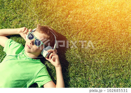 A boy relaxing on grass, listening to music 102685531