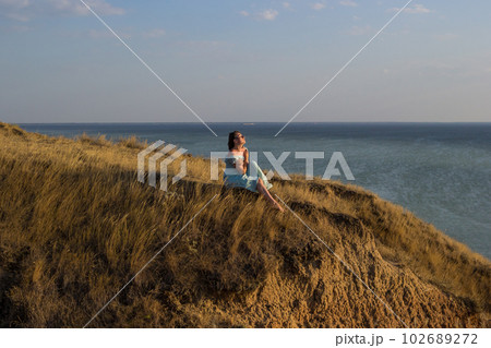 A girl in a long dress sits on a cliff by the sea A girl in a long dress sits on a cliff by the sea 102689272