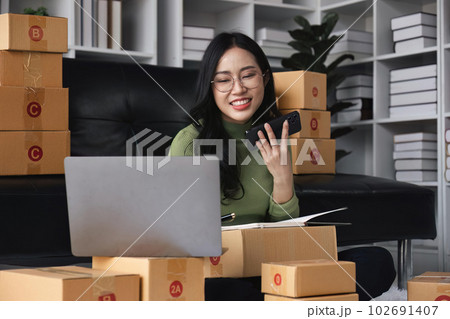 Female small business owner using laptop checking parcel box. Older entrepreneur seller preparing retail package postal shipping order at home 102691407