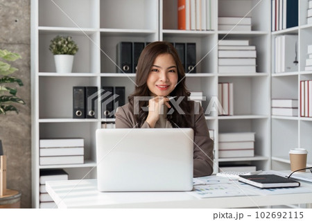 Happy business lady smiling to camera posing working sitting at workplace in office Happy business lady smiling to camera posing working sitting at workplace in office 102692115