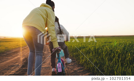 happy family. mother teaches little child to ride bicycle. in the park sunset. chidhood dream. ride a child bike in the sun. happy family life concept. child girl daughter rides road driving bicycle. 102701354