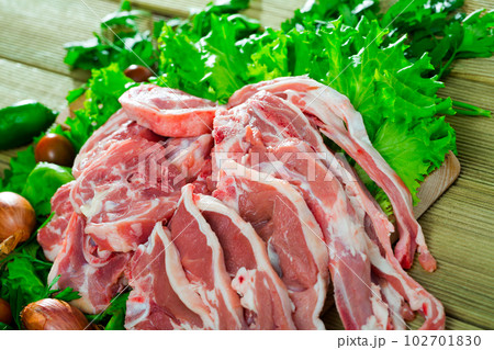 Pieces of fresh lamb meat on a wooden desk with vegetables 102701830