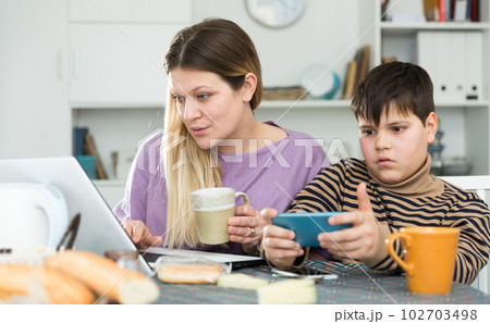 Portrait of young mother and son with tea using gadgets at table 102703498