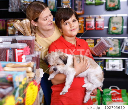 Cheerful woman with preteen son buying dog treats and chews in store to reward their precious pup 102703630